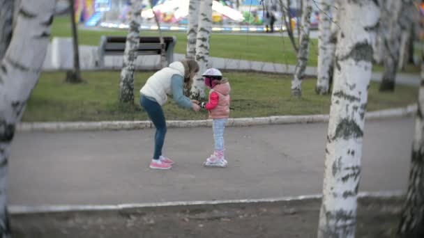 Anya és lánya lovagolni a görkorcsolya. Lány görkorcsolya, és esik a tanulás. Anyuka tanítja a lányát, hogy lovagolni görgőkön — Stock videók