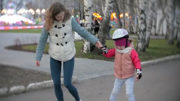 Mom and daughter ride on roller skates. Girl learning to roller skate, and falls. Mom teaches daughter to ride on rollers — Stock Video