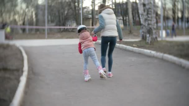 Mom and daughter ride on roller skates. Girl learning to roller skate, and falls. Mom teaches daughter to ride on rollers — Stock Video