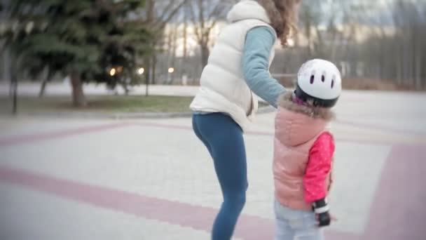 Mom and daughter ride on roller skates. Girl learning to roller skate, and falls. Mom teaches daughter to ride on rollers — Stock Video