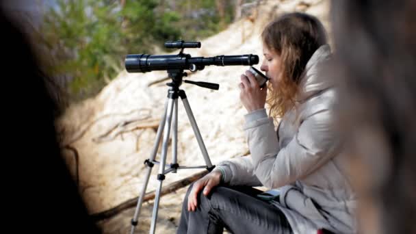 Mujer atractiva mira a través de un telescopio en un bosque en la orilla del río — Vídeo de stock