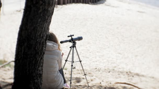 Attractive woman looks through a telescope in a forest on the river bank — Stock Video