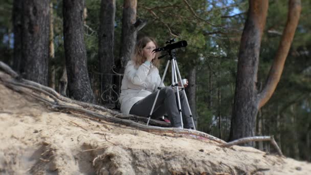 Mujer atractiva mira a través de un telescopio en un bosque en la orilla del río — Vídeo de stock