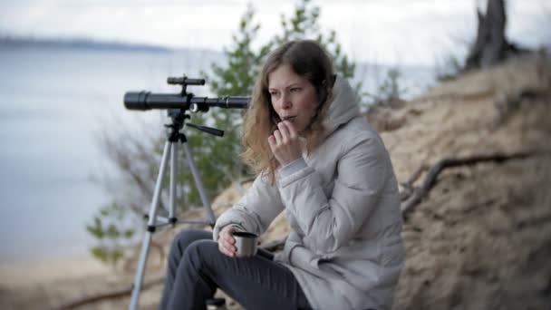 Attractive woman looks through a telescope in a forest on the river bank — Stock Video