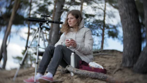 Donna attraente guarda attraverso un telescopio in una foresta sulla riva del fiume — Video Stock