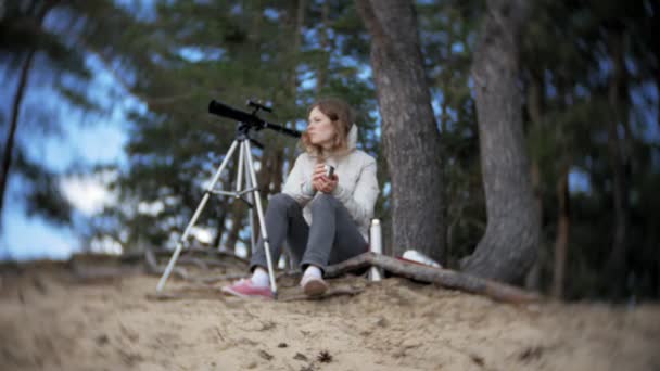 Ελκυστική γυναίκα κοιτάζει μέσα από τηλεσκόπιο σε ένα δάσος στην όχθη του ποταμού — Αρχείο Βίντεο