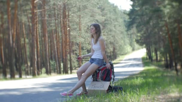 年轻美丽的女子搭便车站在路上, 一个背包在一个表与一个题词南 — 图库视频影像