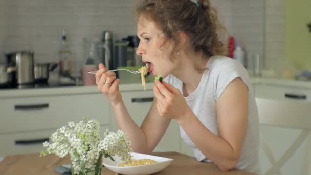 Una hermosa mujer joven comiendo pasta de pollo parmesano en la cocina casera — Vídeos de Stock