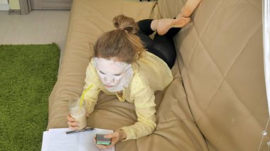 Genç kadının temizlik maskesi, yüz maskesi maskesi yapması tıklama ile smartphone evde kanepede