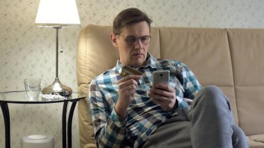 Online satın alma bir adam bir telefon ve bir kredi kartı kullanan kanepede eve yaşam tarzı akıllı iş internet teknoloji banka bankacılık para tutan cep telefonu istemci closeup aygıt el alışveriş