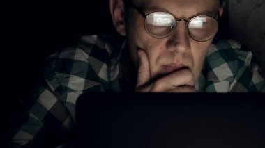 Gözlüklü bir adam gece geç saatlerde çalışıyor. Önünde bir yakın çekim bilgisayar ekranında gördüğü endişeli görünüyor,