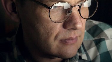 Gözlüklü bir adam gece geç saatlerde çalışıyor. Önünde bir yakın çekim bilgisayar ekranında gördüğü endişeli görünüyor,