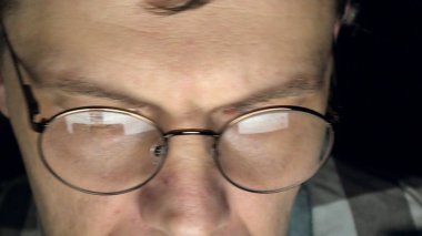 Gözlüklü bir adam gece geç saatlerde çalışıyor. Önünde bir yakın çekim bilgisayar ekranında gördüğü endişeli görünüyor,