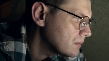 Gözlüklü bir adam gece geç saatlerde çalışıyor. Önünde bir yakın çekim bilgisayar ekranında gördüğü endişeli görünüyor,