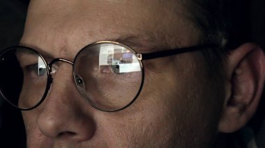 Gözlüklü bir adam gece geç saatlerde çalışıyor. Önünde bir yakın çekim bilgisayar ekranında gördüğü endişeli görünüyor,