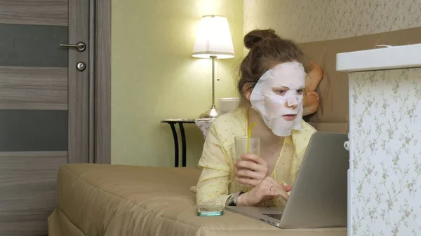 Ung kvinna gör ansiktsmask mask med rengörande mask, arbetar bakom laptop hemma — Stockfoto