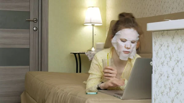 Ung kvinna gör ansiktsmask mask med rengörande mask, arbetar bakom laptop hemma — Stockfoto