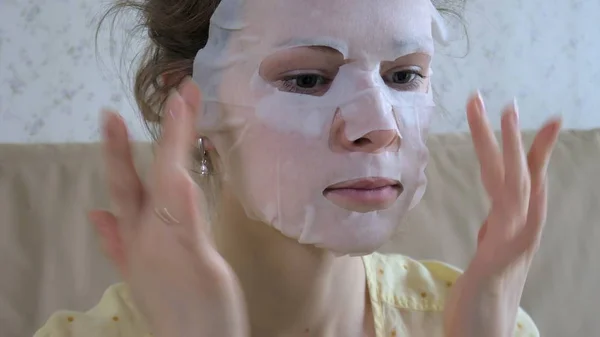 Young woman doing facial mask mask with cleansing mask on face in kitchen at home — Stock Photo, Image