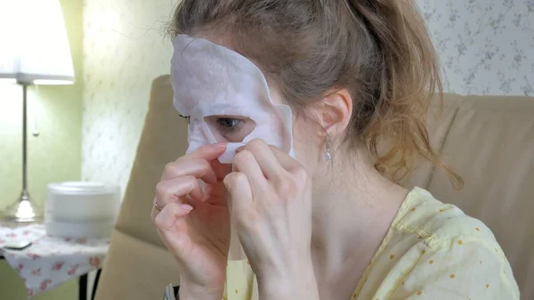 Jonge vrouw doet facial mask masker met zuivering masker op gezicht in keuken thuis — Stockfoto