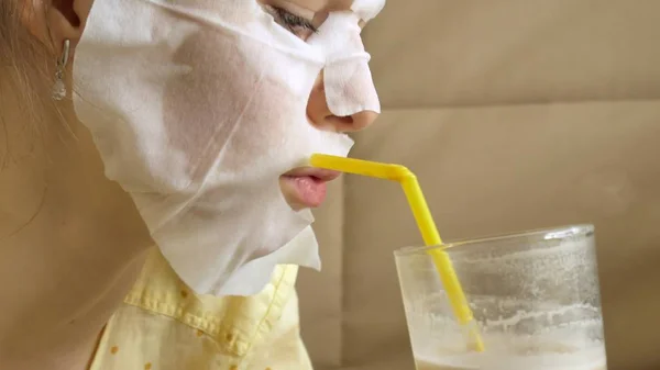 Mujer joven haciendo máscara facial con máscara de limpieza, clics en el sofá con teléfono inteligente en casa — Foto de Stock