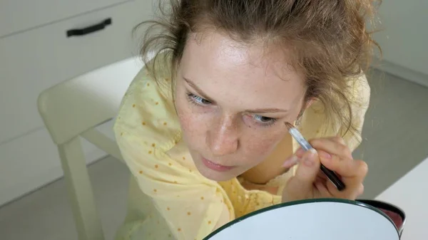 Jovem mulher bonita fazendo maquiagem na frente de um espelho em casa . — Fotografia de Stock