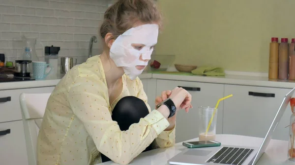 Jeune femme faisant masque facial masque avec masque nettoyant, travaillant derrière un ordinateur portable à la maison — Photo