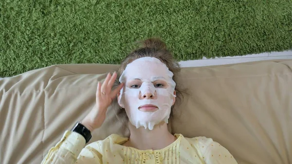 Jeune femme faisant masque facial masque avec masque nettoyant, clique sur le canapé avec smartphone à la maison — Photo