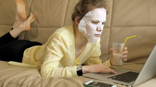 Junge Frau macht Gesichtsmaske mit Reinigungsmaske, arbeitet zu Hause hinter Laptop — Stockfoto