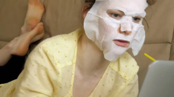 Mujer joven haciendo máscara facial con máscara de limpieza, trabajando detrás de la computadora portátil en casa — Foto de Stock