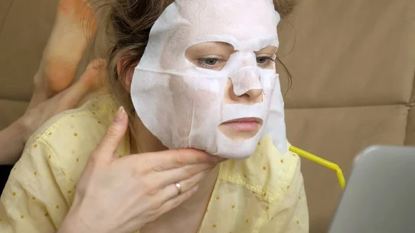 Mujer joven haciendo máscara facial con máscara de limpieza, trabajando detrás de la computadora portátil en casa —  Fotos de Stock