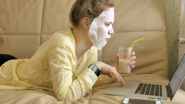 Молодая женщина делает маску для лица с очищающей маской, работает за ноутбуком дома — стоковое фото