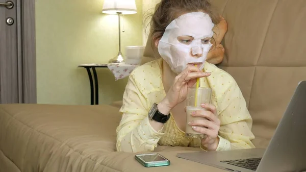 Mujer joven haciendo máscara facial con máscara de limpieza, trabajando detrás de la computadora portátil en casa —  Fotos de Stock