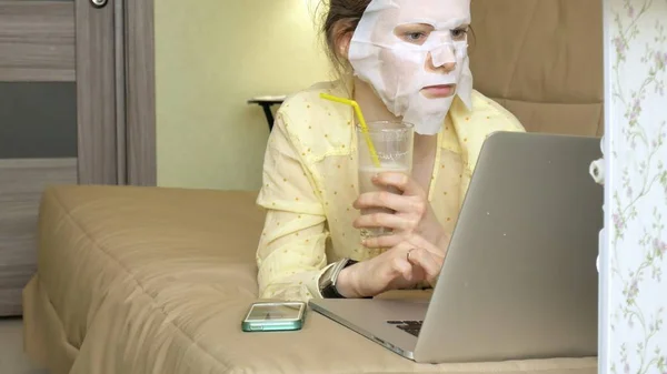 Ung kvinna gör ansiktsmask mask med rengörande mask, arbetar bakom laptop hemma — Stockfoto