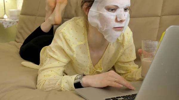 Junge Frau macht Gesichtsmaske mit Reinigungsmaske, arbeitet zu Hause hinter Laptop — Stockfoto