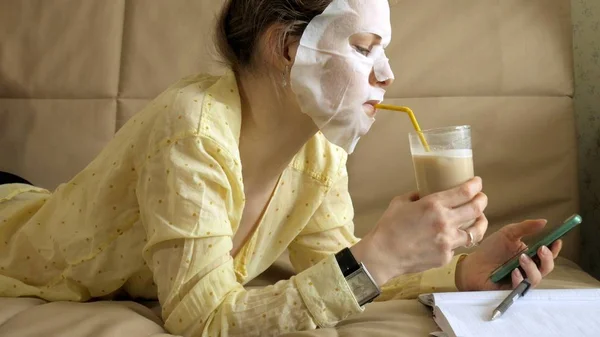 Mladá žena, která dělá maska maska s čistící masku, klepne na gauči s smartphone doma — Stock fotografie