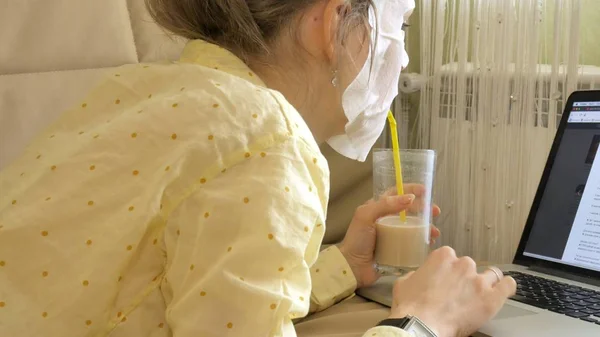 Jonge vrouw doet gezichtsmasker met zuivering masker, masker werken achter een laptop thuis — Stockfoto