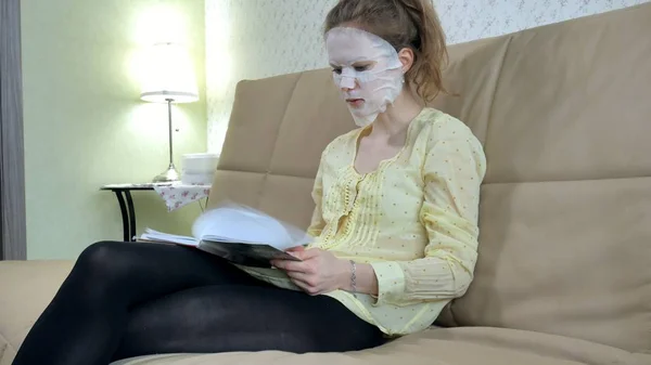 Jeune femme faisant masque facial masque avec masque nettoyant, clique sur le canapé avec smartphone à la maison — Photo