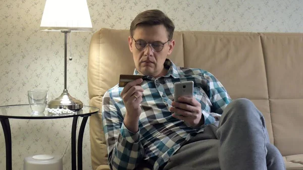 Online satın alma bir adam bir telefon ve bir kredi kartı kullanan kanepede eve yaşam tarzı akıllı iş internet teknoloji banka bankacılık para tutan cep telefonu istemci closeup aygıt el alışveriş