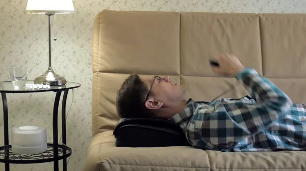 Homem deita-se no sofá em casa, sob a cabeça de um massageador, estado relaxado — Fotografia de Stock