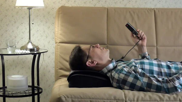 Homme couché sur le canapé à la maison, sous la tête d'un masseur, état détendu — Photo