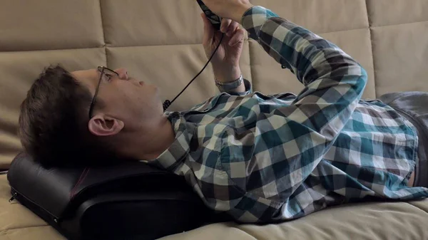 Férfi fekszik a kanapén, otthon, alatt a feje a masszírozó, nyugodt állapotban — Stock Fotó