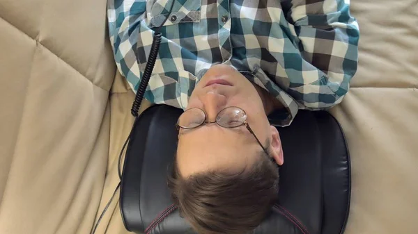 Mann liegt zu Hause auf der Couch, unter dem Kopf eines Massagegeräts, entspannter Zustand — Stockfoto