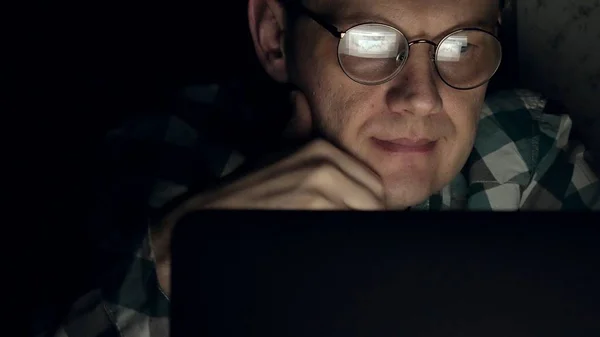 Ένας άνδρας με γυαλιά που λειτουργεί αργά τη νύχτα. Αυτός φαίνεται ανήσυχος, βλέπει στην οθόνη του υπολογιστή μπροστά του, μια στενή-up — Φωτογραφία Αρχείου