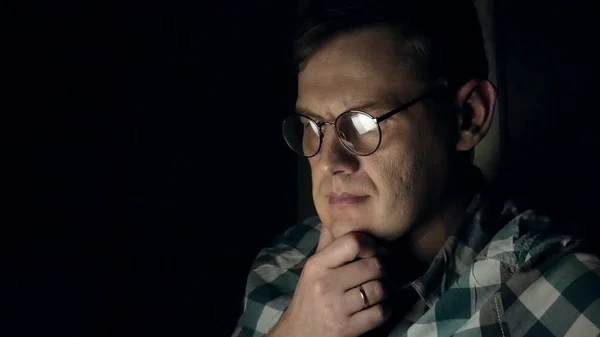 Człowiek w okularach działa późno w nocy. Wygląda on martwi się, on widzi na ekranie komputera przed nim, zbliżenie — Zdjęcie stockowe