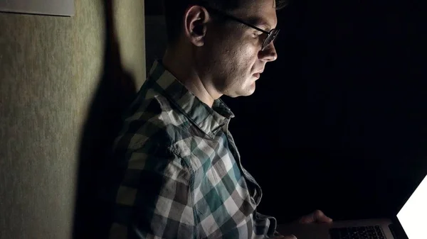 Un homme à lunettes travaille tard dans la nuit. Il a l'air inquiet, il voit sur l'écran de l'ordinateur devant lui, un gros plan — Photo