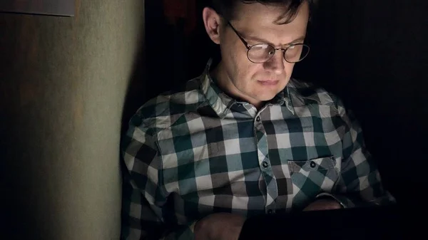 Un homme à lunettes travaille tard dans la nuit. Il a l'air inquiet, il voit sur l'écran de l'ordinateur devant lui, un gros plan — Photo