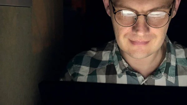 A man in glasses works late at night. He looks worried, he sees on the computer screen in front of him, a close-up — Stock Photo, Image