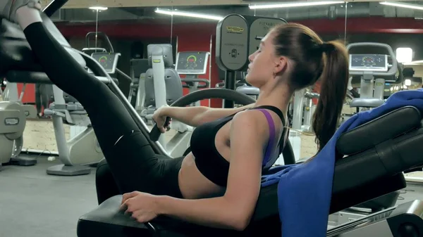 Una mujer atractiva hace estiramiento en un simulador en un gimnasio deportivo —  Fotos de Stock