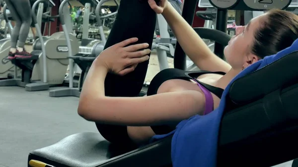 Una mujer atractiva hace estiramiento en un simulador en un gimnasio deportivo —  Fotos de Stock