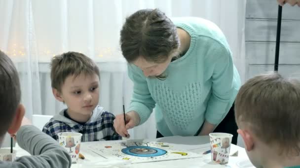 Barn pojkar sitter tillsammans runt bordet i klassrummet och rita. Med dem är deras unga och vackra lärare. — Stockvideo